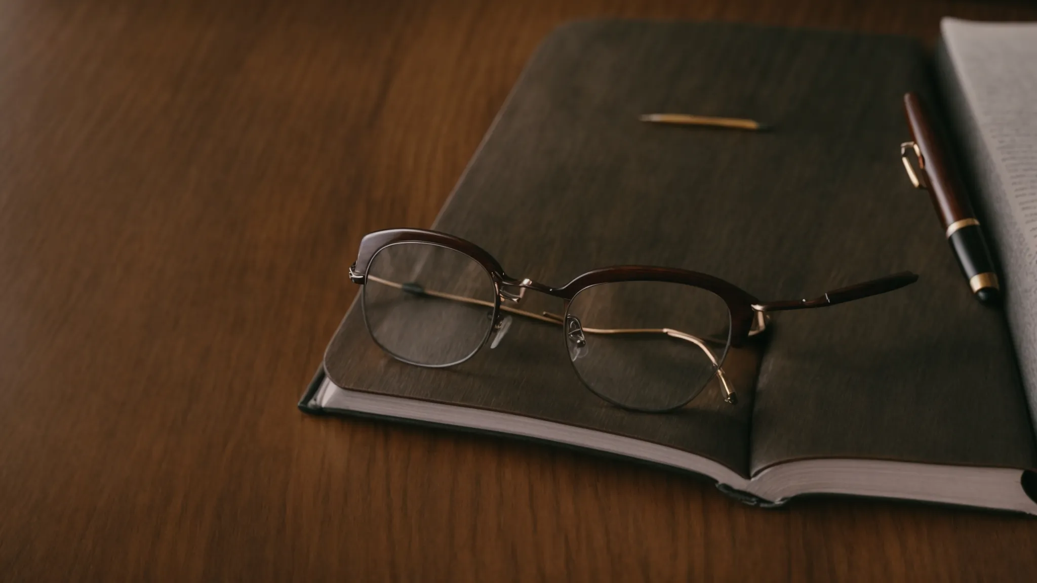 a pair of glasses resting on an open book, with a pen laid alongside atop a wooden desk.