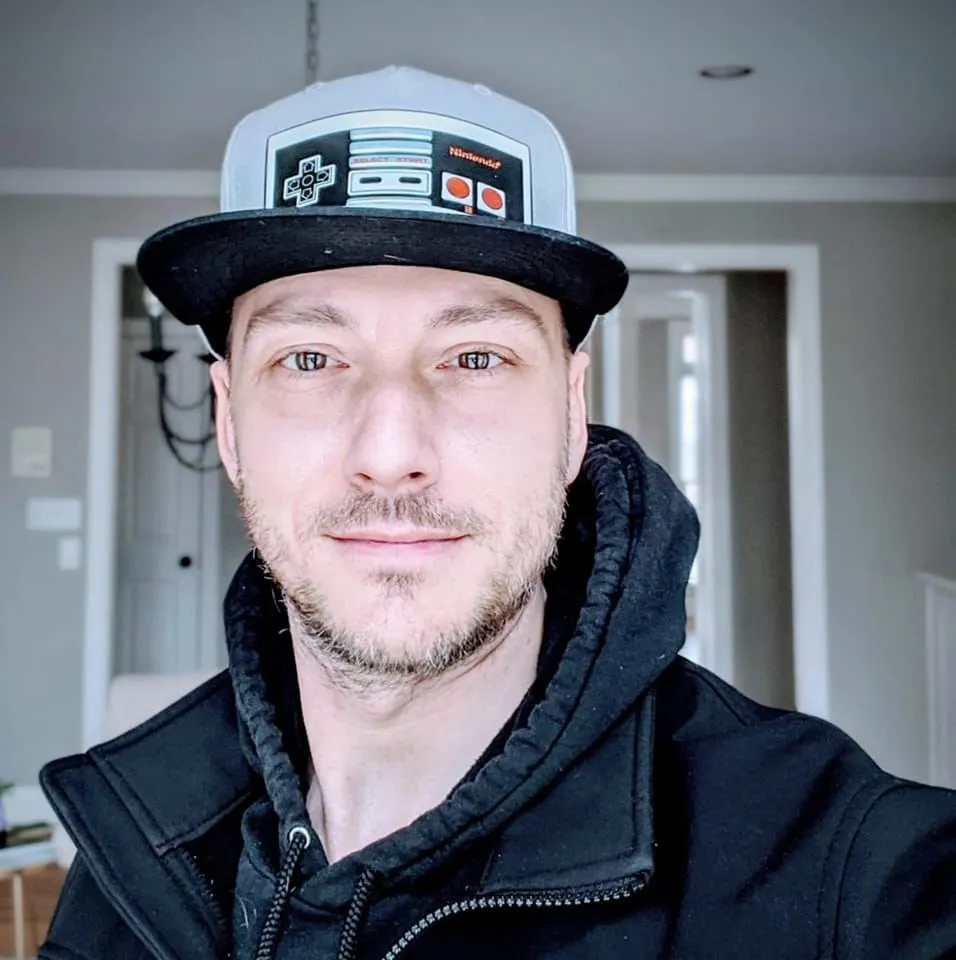 A person wearing a cap with a classic video game controller design is smiling at the camera in this engaging video testimonial.