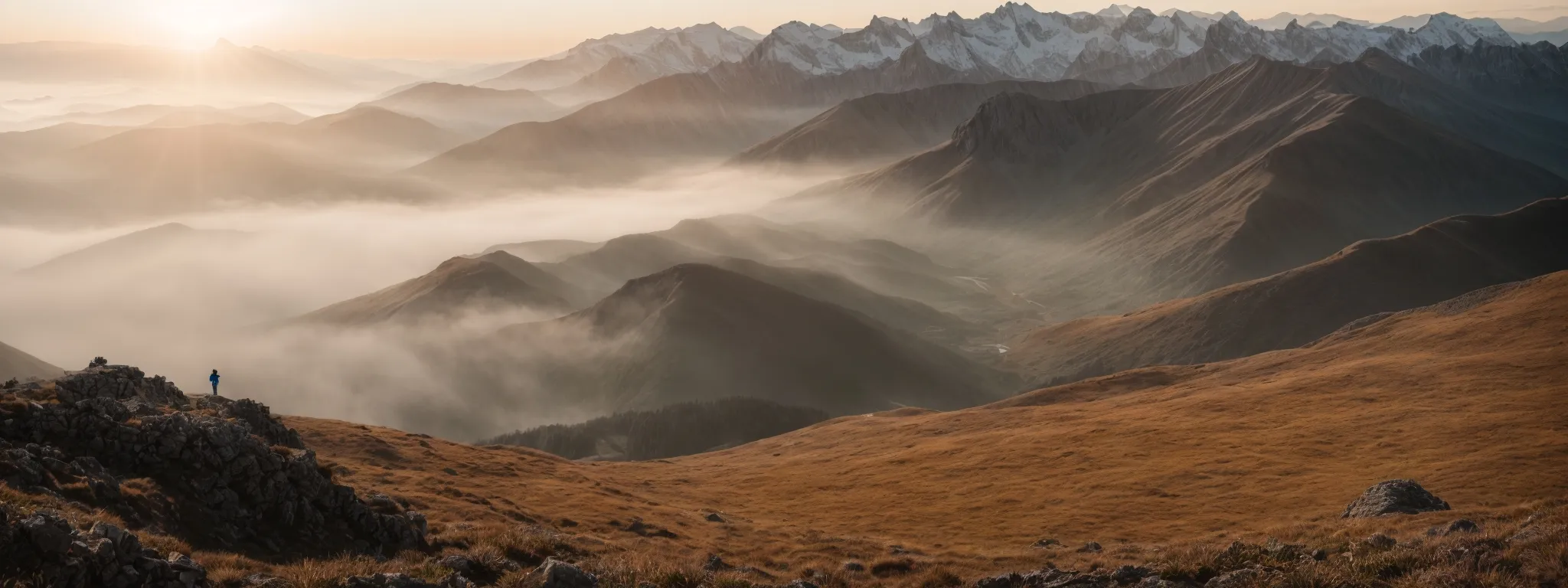 a panoramic view of a mountaineer on a peak overlooking a vast, unexplored landscape bathed in the soft glow of dawn.