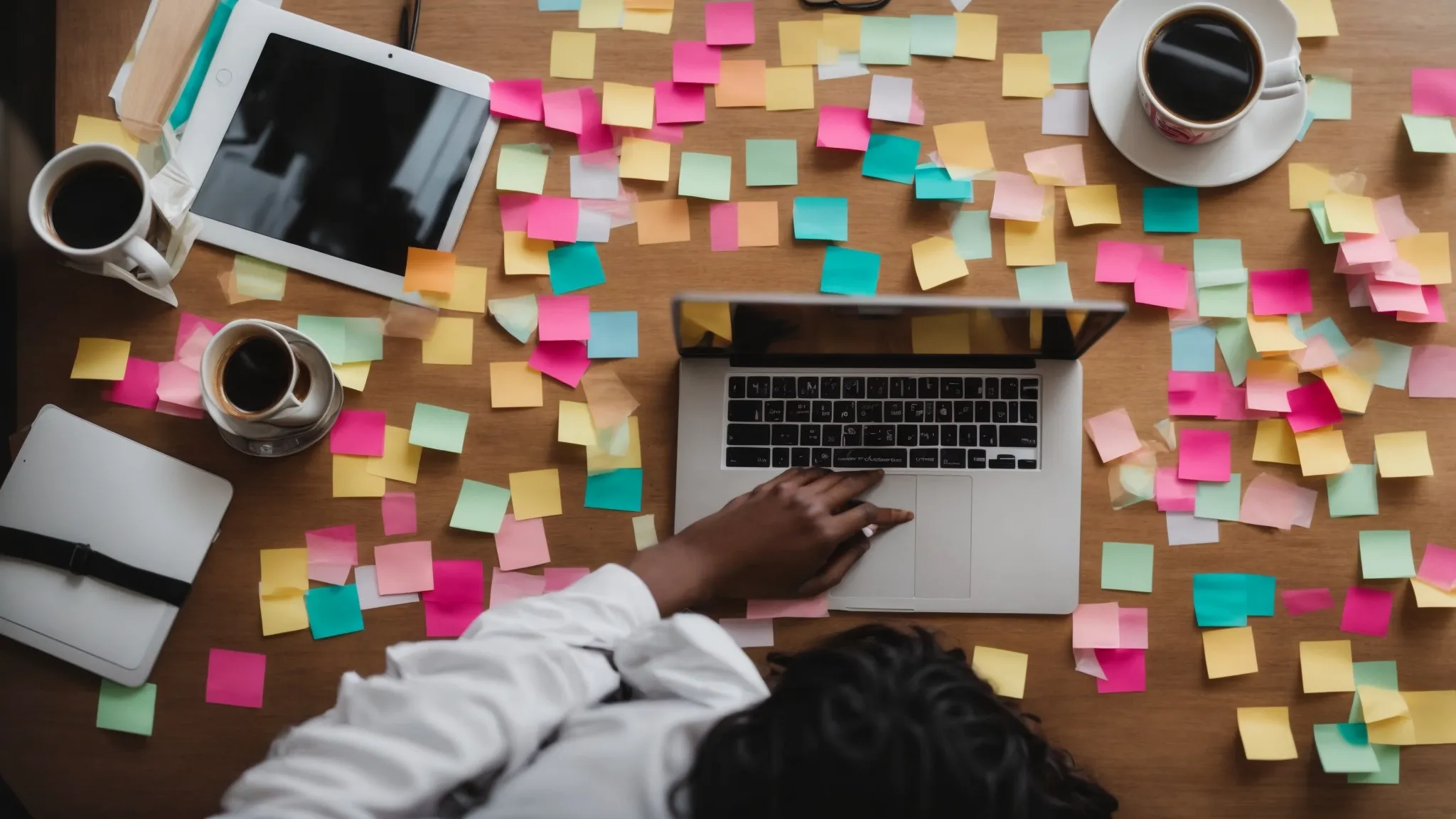 a person typing on a laptop surrounded by colorful sticky notes with keywords and a cup of coffee nearby.
