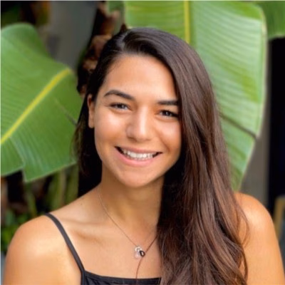 Smiling woman with long dark hair, wearing a black top, stands in front of large green leaves, highlighting her natural beauty much like the intuitive design of OTTO's latest feature for SEO optimization.